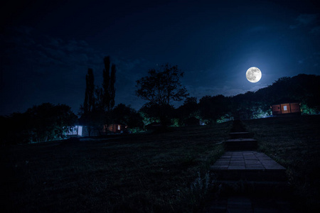 夜晚用月亮或老式乡村住宅在森林中建造的山夜景观，夜晚用云彩和星星。 夏夜。 长时间曝光拍摄的照片