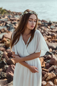 美丽的年轻温柔的女人在岩石海滩上摆着花圈