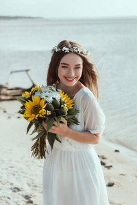 美丽的快乐女孩穿着白色连衣裙，手里拿着沙滩上的向日葵