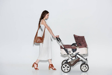 女性侧景，穿着时尚的白色连衣裙，在灰色的婴儿车上行走。