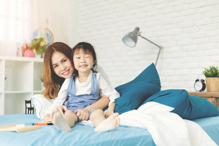快乐的亚洲家庭母亲和她的女儿在家里的床上笑着。