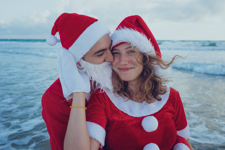 幸福的一对夫妇穿着圣诞老人的服装在海滩上散步。 圣诞节假期的概念。
