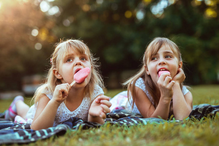 两个快乐的金发姐妹在公园里吃冰淇淋的肖像。