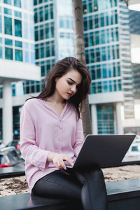 一位年轻的女商人在外面使用笔记本电脑，一位漂亮的忙碌的女士在电脑上工作，女经理在电脑键盘上打字，坐在她办公室附近的工作过程概念