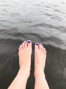美丽的女性脚与手指与多色时尚的指甲被丢弃悬在冰冷的黑水中