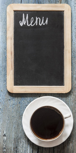 俯视并关闭。 一个空的小黑板给你的课文，一杯热咖啡在木制背景上