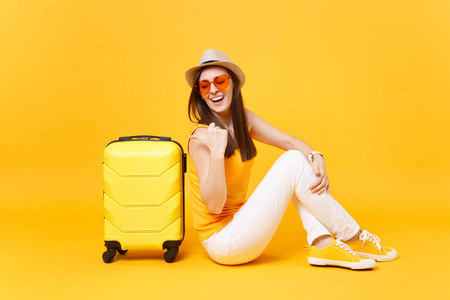 旅行者旅游妇女戴着夏季休闲服装帽，坐在黄色橙色背景上的手提箱上。 女乘客在周末出国旅行，度假。 航空旅行概念