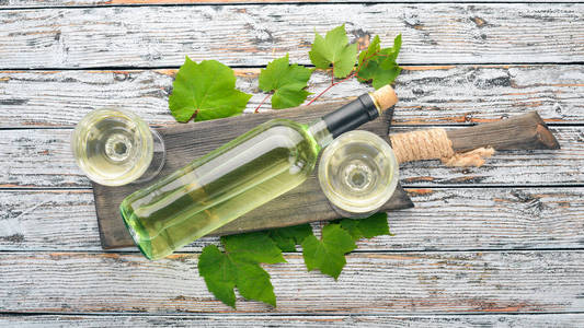 白葡萄酒在一个瓶子里，有一个杯子和葡萄。 在白色的木制背景上。 免费的文本空间。 上面的风景。