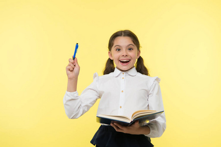 女孩可爱的女生在制服举行书籍或教科书黄色背景。勤奋的学生从书本上获得知识。孩子穿校服准备课她的知识。对知识的兴奋