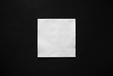 空白白纸餐巾在黑色背景上，有复制空间。 平躺着。