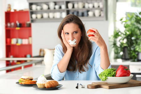 厨房里有胶带嘴和不同产品的女人。 健康和不健康食品之间的选择