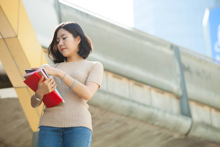 美丽的亚洲女大学生拿着她的书，微笑着，快乐地站在户外，人们教育学习，高中项目，聪明的青少年概念