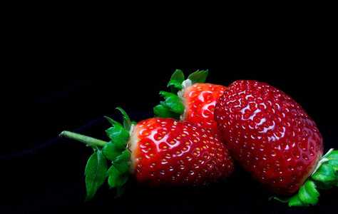 接近三个新鲜草莓的黑色背景，有用的维生素新鲜，素食饮料和食谱草莓