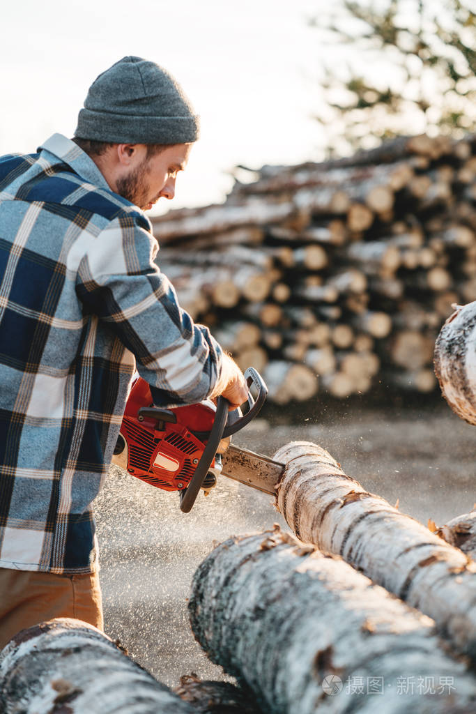 长胡子的野蛮伐木工人穿着格子衬衫,用电锯锯树,在锯木厂工作.