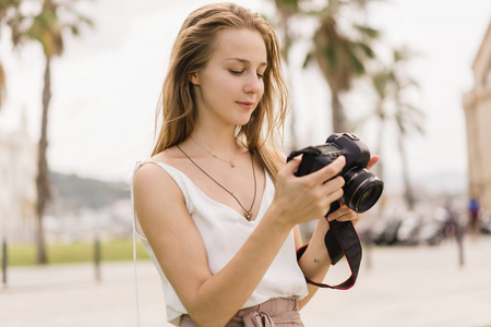 漂亮的微笑女孩在DSLR相机上拍照，并检查屏幕上的设置。 专业女摄影师旅行者在公园的照片相机上拍摄。 户外夏季绿色公园