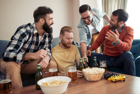 友谊科技游戏和家庭概念微笑男性朋友喝啤酒，在家玩电子游戏。