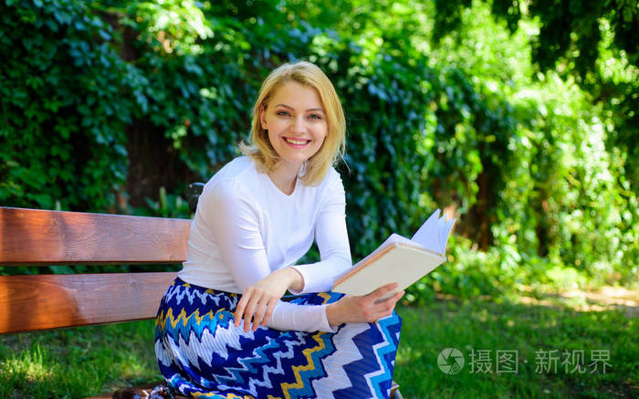 女人快乐微笑金发女郎休息放松在花园看书.