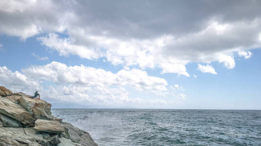 坐在岩石悬崖上观察大海的孤独女孩