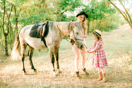 一个漂亮的小女孩，穿着一件老式的格子连衣裙，戴着一顶草帽，还有一匹灰色的马，浅卷发。 秋天的农村生活。 马和人