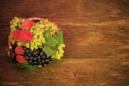 碗里放着葡萄，秋天的叶子放在古老的木制背景上