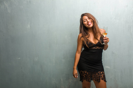 年轻漂亮女人的肖像，穿着一件连衣裙靠墙，表达自信和情感，乐趣和友好的舌头，作为游戏或乐趣的标志。 拿着香槟杯。