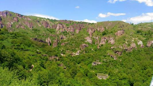 阿尔梅尼亚洞穴小镇卡恩佐尔斯克的高加索山脉在岩石中淹没在绿色的植被中，蓝天上乌云密布