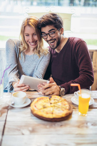 微笑的夫妇享受比萨饼，一起玩和使用平板电脑。