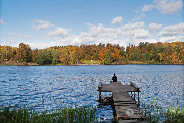 阳光明媚的秋日,孤独的人坐在湖边的码头上照片-正版商用图片131m4y