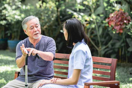 护士和病人坐在长凳上一起说话。 亚洲老人和年轻女子坐在一起说话。 放松心情。