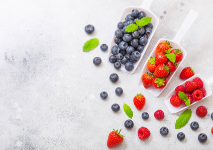 厨房桌子上白色勺子里新鲜的生有机浆果。 文本空间。 上面的风景。 草莓覆盆子蓝莓和薄荷叶