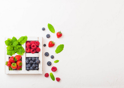 厨房桌子背景上白色木箱中的新鲜生有机浆果。 文本空间。 草莓覆盆子蓝莓和薄荷叶