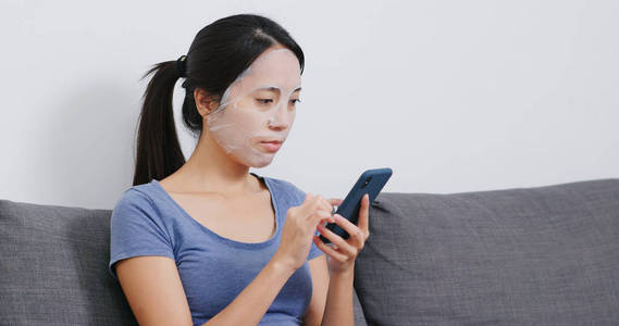 妇女使用手机，并在家里敷纸面具