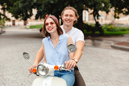 一对幸福的年轻夫妇一起骑摩托车在城市街道上的画像