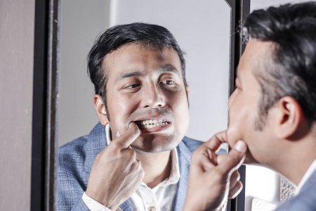 亚洲男人穿西装，在镜子前照顾他的外表，美容造型的生活方式。