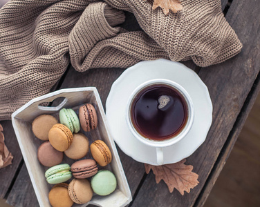 一杯热茶，马卡龙，木桌上的针织毛衣。 秋天。 很舒服。