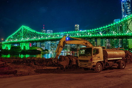 夜间布里斯班发光桥和摩天大楼背景上泥土的现场挖掘机