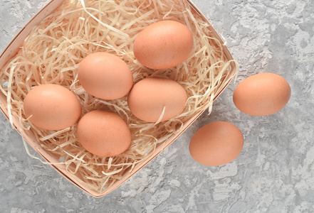 许多鸡蛋放在篮子里，稻草放在灰色的混凝土表面上