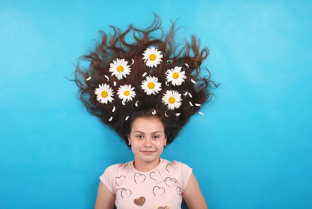 一个年轻女孩的肖像，头发上有雏菊，躺在地板上，蓝底画室