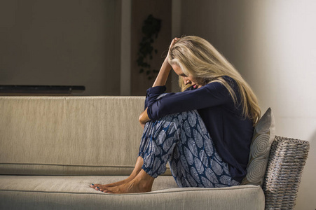 40岁沮丧焦虑的美丽金发女郎抑郁头痛沮丧坐在家里的沙发上，在中年危机和生活问题上悲伤绝望