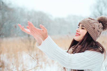 快乐的女人在白雪皑皑的冬天公园的散步中捕捉雪花。 户外季节性活动的概念