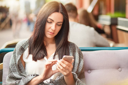 严肃的黑发女人在现代手机上阅读收入信息，穿着随意，手持现代手机接收短信类型，反馈意见，照片在社交网络中。 休闲概念