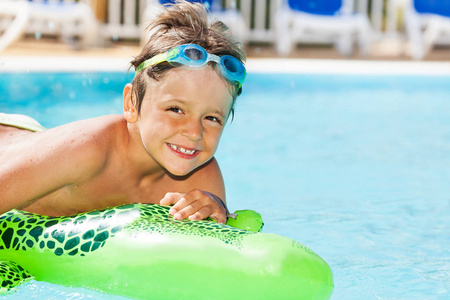亲密的肖像快乐的男孩在护目镜游泳与充气玩具在游泳池