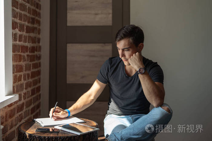 有思想的人写笔记本电脑旁边的平板电脑坐在桌子旁,在房间里工作,在