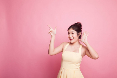 兴奋的亚洲女人指着粉红色背景上的空白