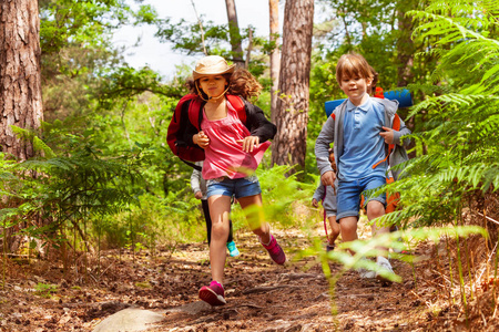 一群男孩和女孩在森林里快乐地奔跑，微笑着穿着休闲装背包露营
