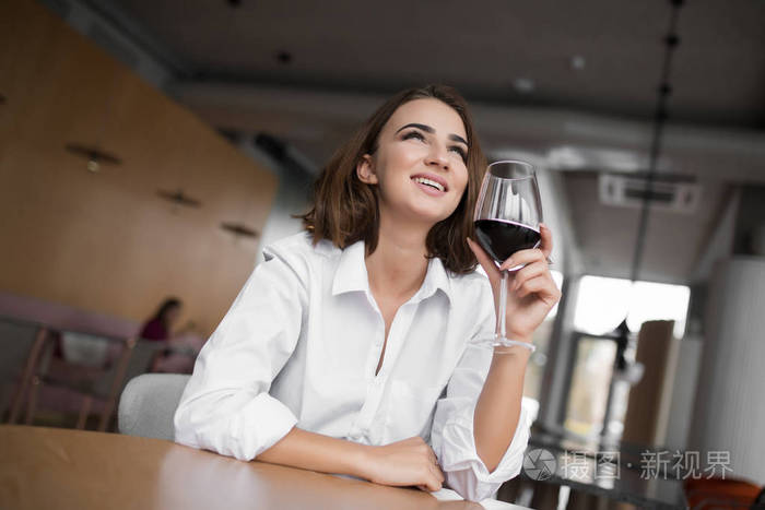 年轻微笑的女人端着红酒杯坐在餐厅里