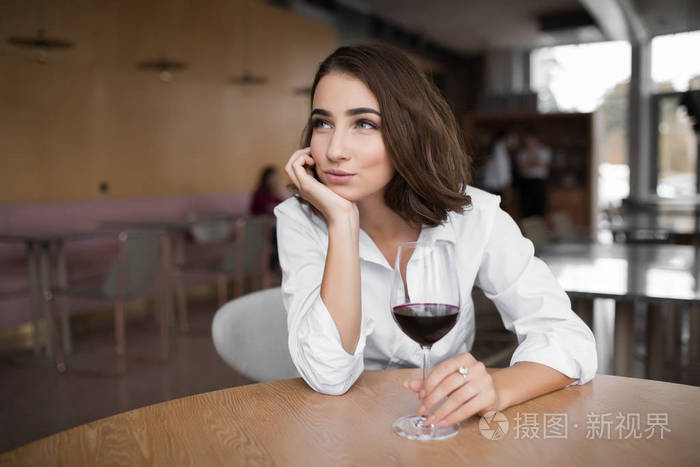年轻女子端着红酒杯坐在餐厅里,头靠在手上