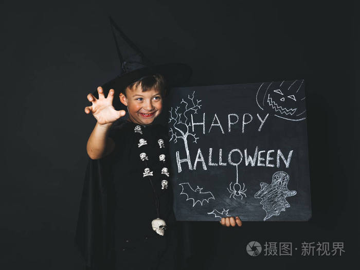 微笑的男孩穿着魔术师的服装,黑色斗篷拿着快乐的万圣