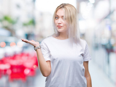 年轻的金发女人在孤立的背景上微笑，欢快的呈现，用手掌指着相机。