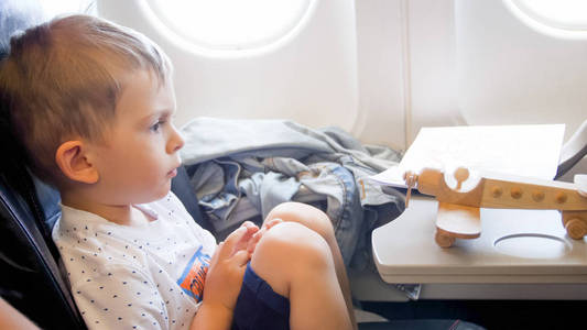 特写色调的可爱的蹒跚学步的男孩坐在飞机上, 看着小玩具双的照片